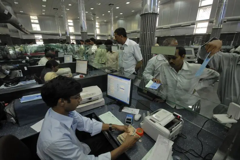 A buys banking center in India. We can see a teller at the desk counting money from the client